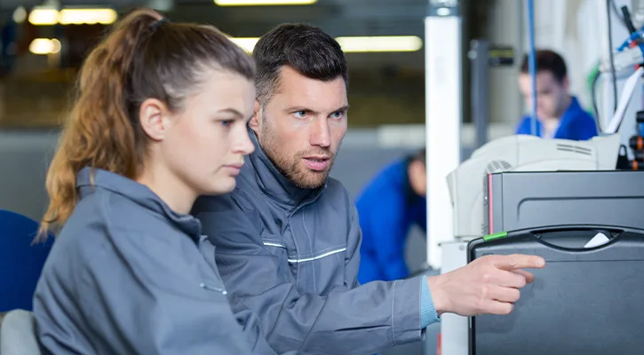 junge-frau-sitzt-am-computer-mit-mann-der-ihr-etwas-erklährt